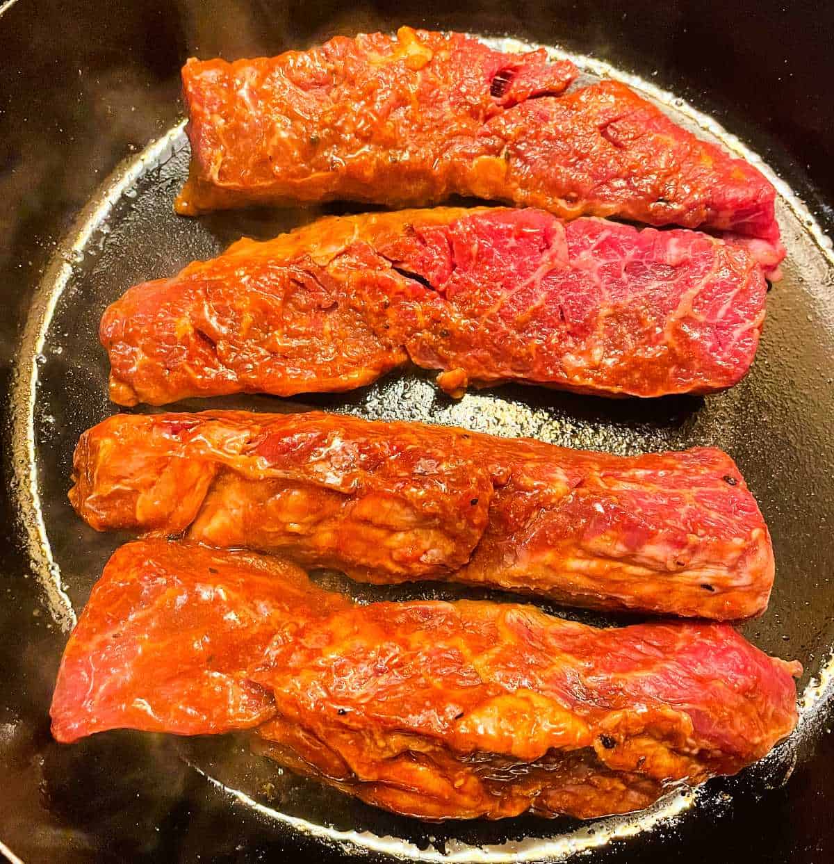 steak tips getting seared in a black cast iron skillet.