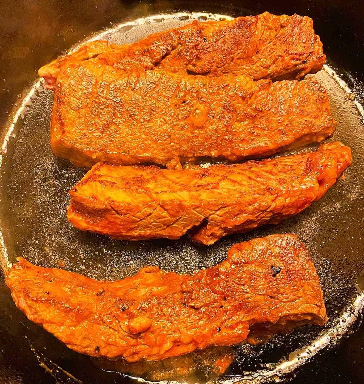 steak tips getting browned in a black cast iron skillet.