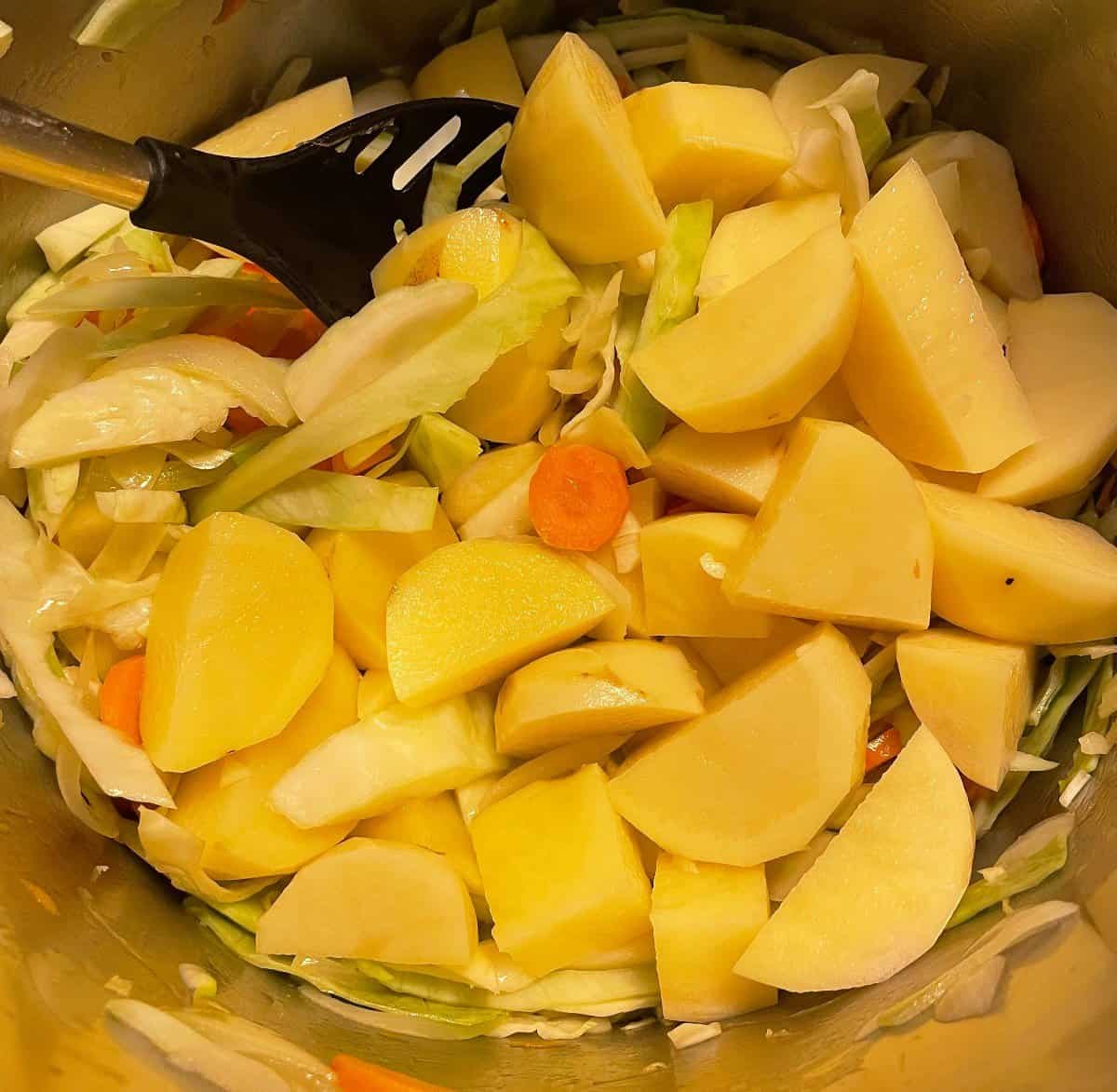 adding potatoes to a soup pot with cabbage and carrots.