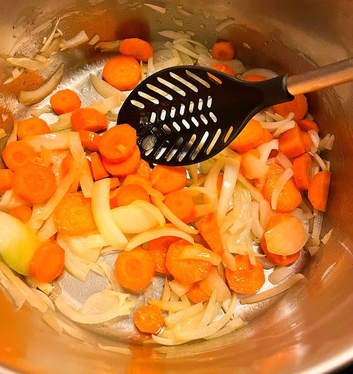 stirring sliced carrots and onions in a large silver soup pot.