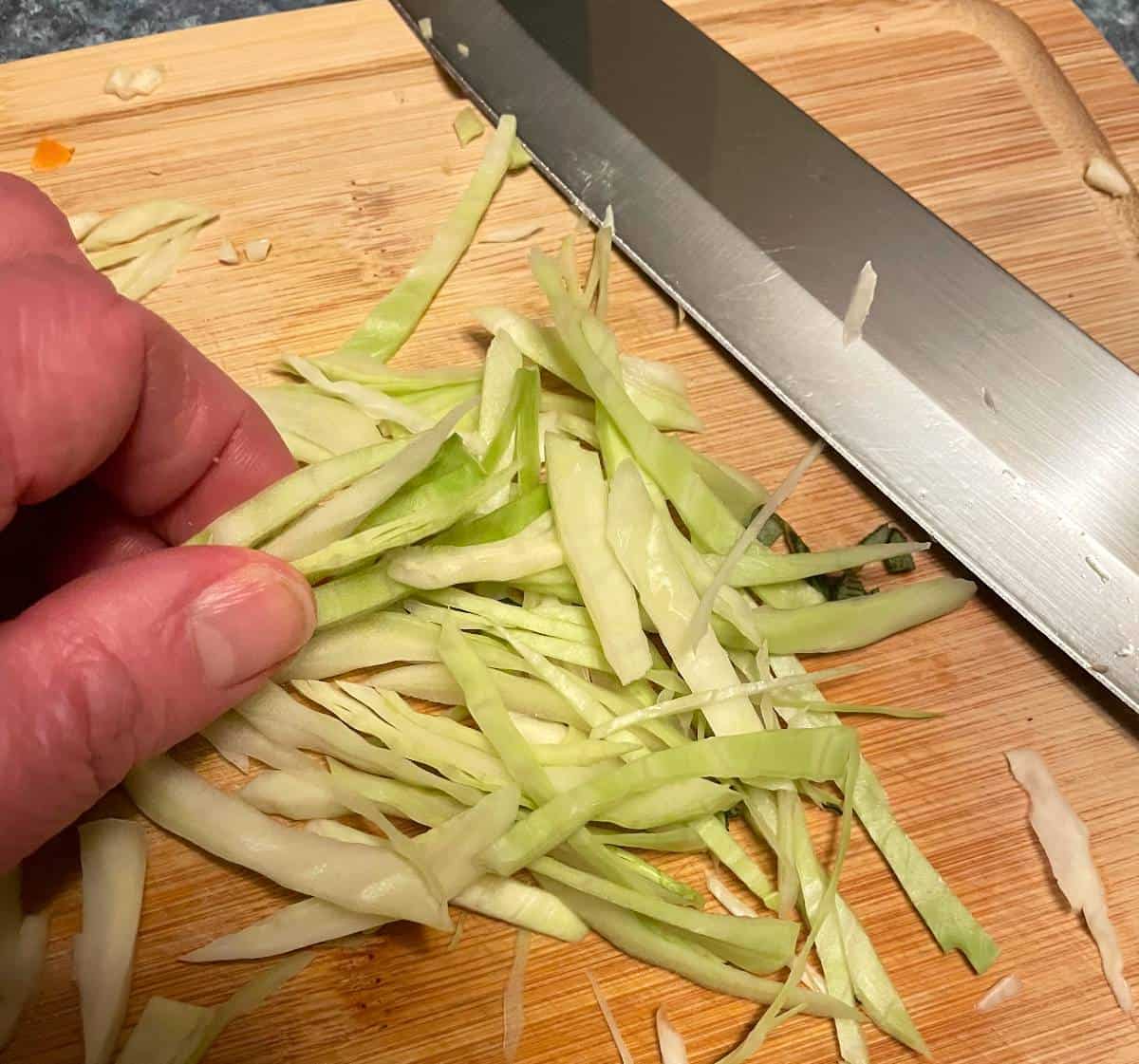 chopping green cabbage on a wooden cutting board.