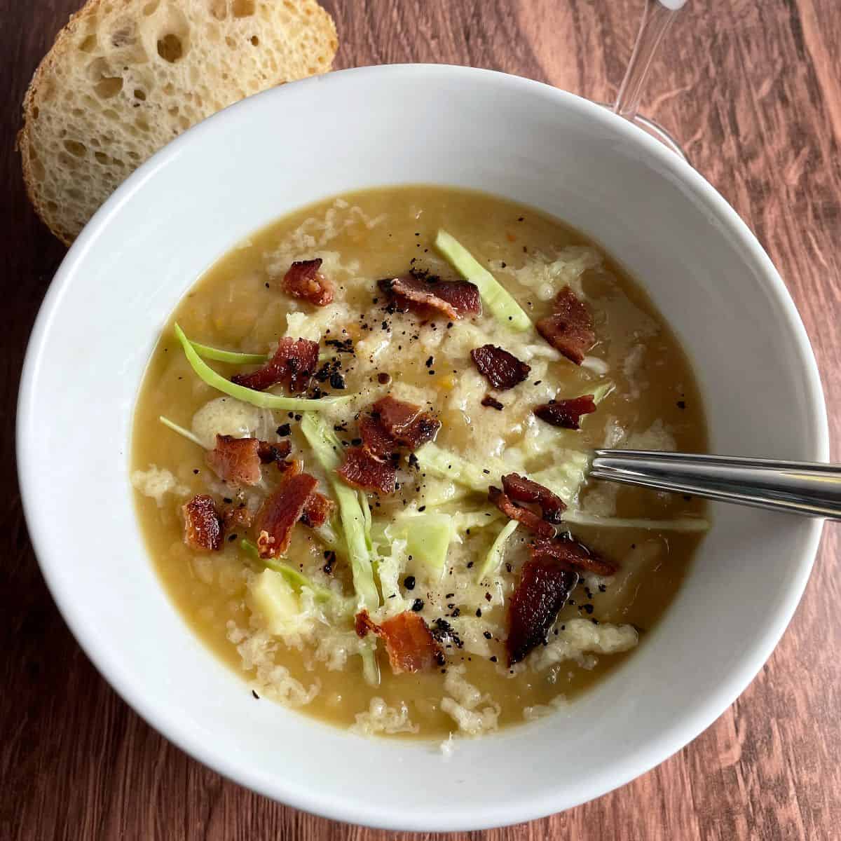 Irish potato soup topped with bacon, cheddar and cabbage, served in a white bowl.