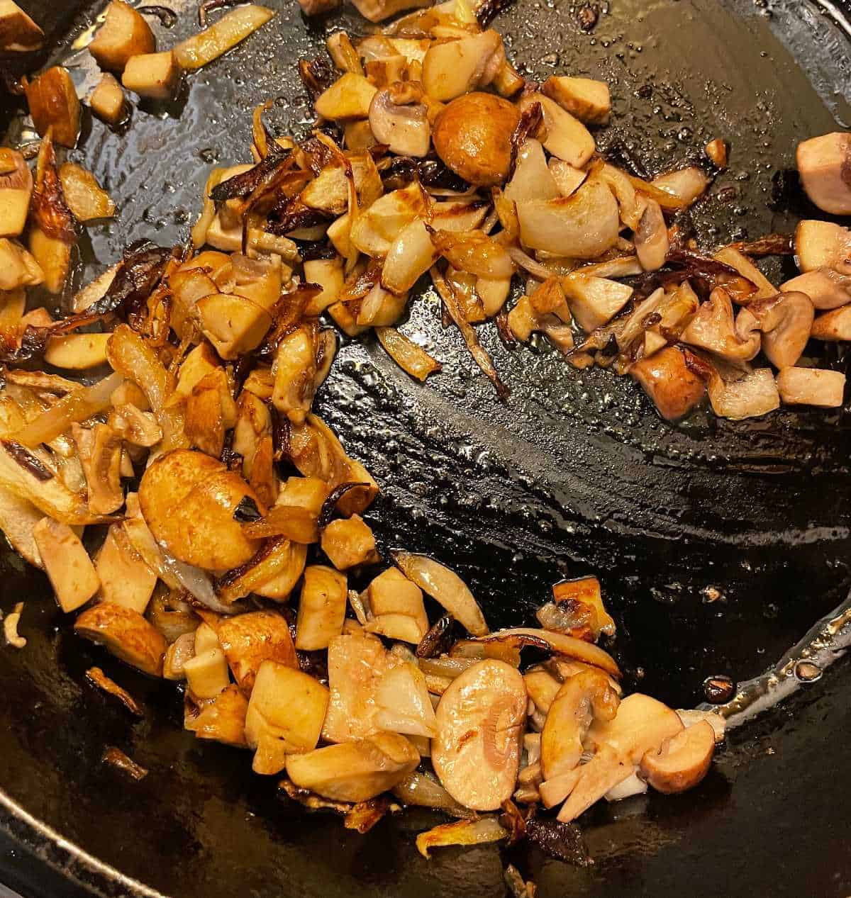 mushrooms and onions cooking in a black skillet.