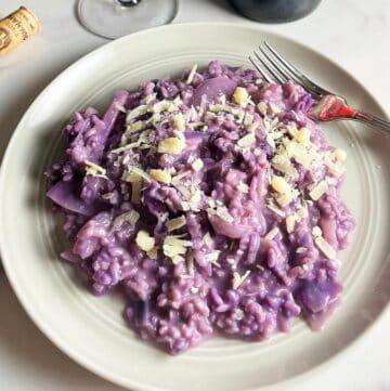 red cabbage risotto topped with cheese and served on an off white plate.
