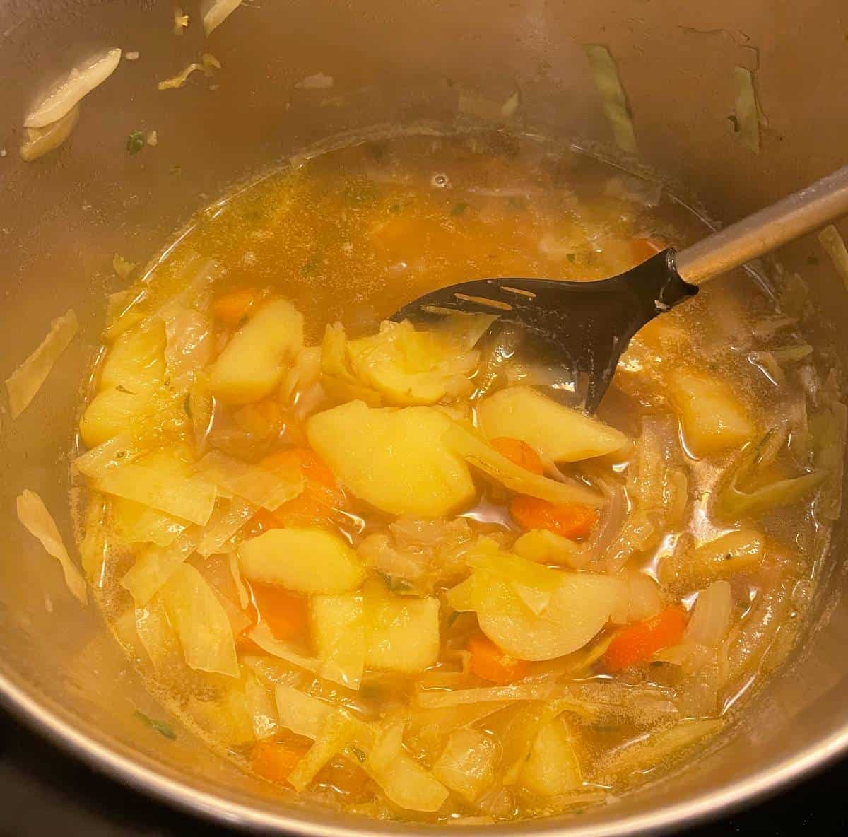 stirring a pot of Irish potato soup with carrots and cabbage.