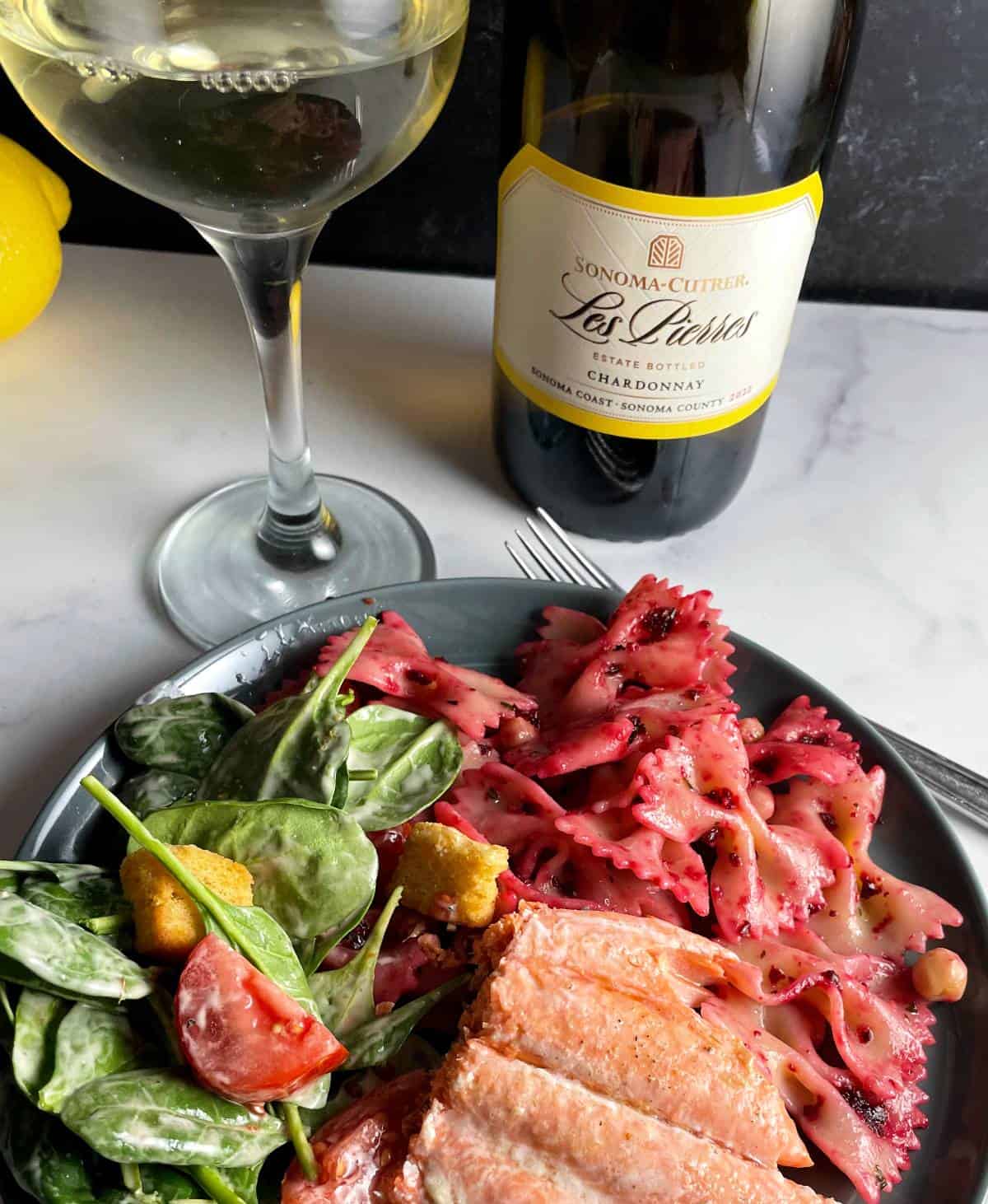 roasted beet pesto pasta plated with salmon and a salad, and served with a Chardonnay wine.