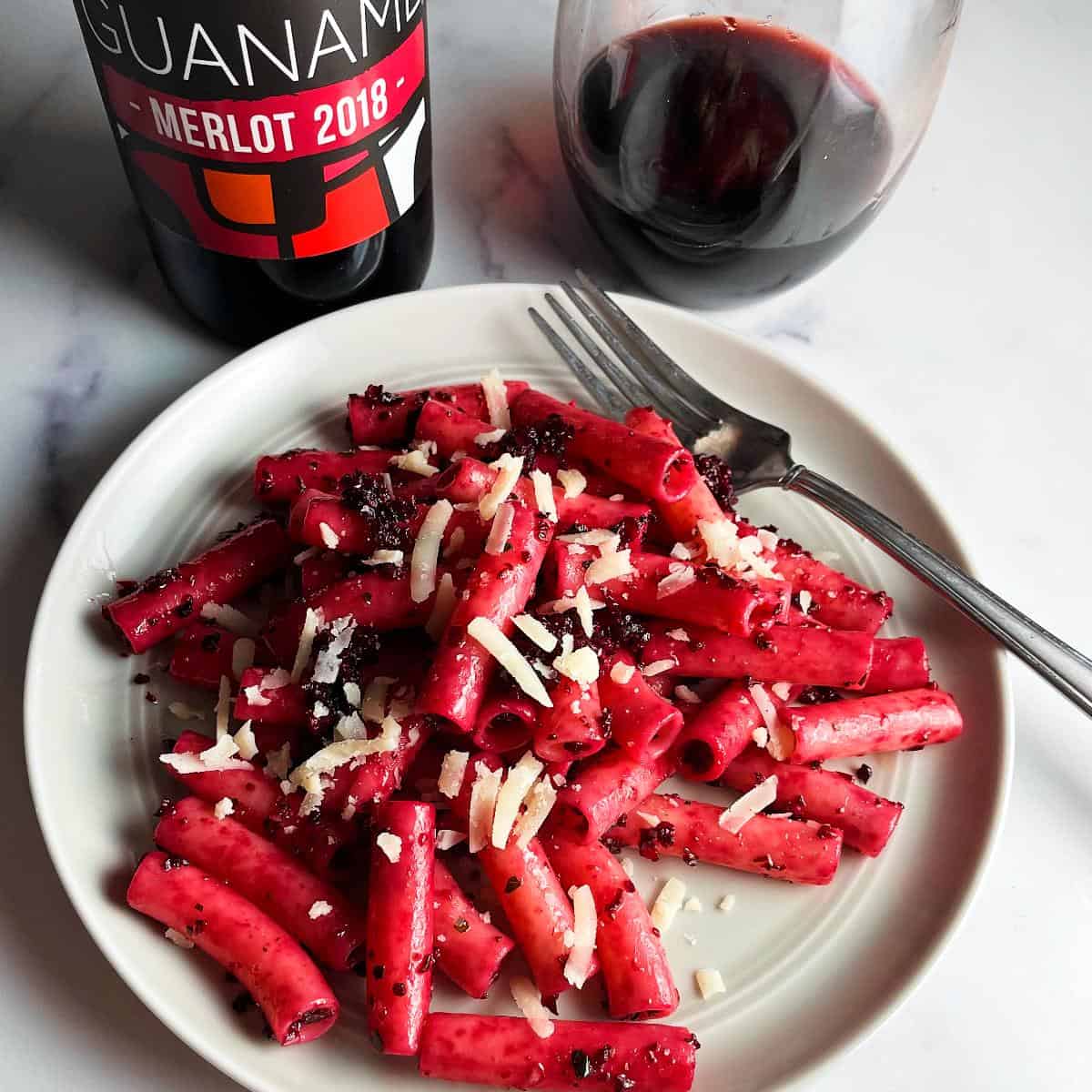 roasted beet pesto pasta on a gray plate, served with a red wine.
