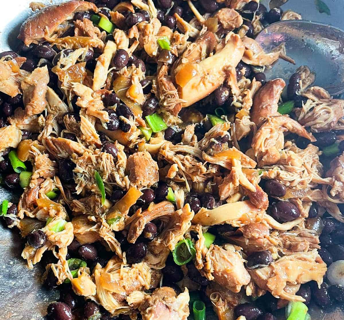 shredded chicken with scallions and black beans in a silver bowl.