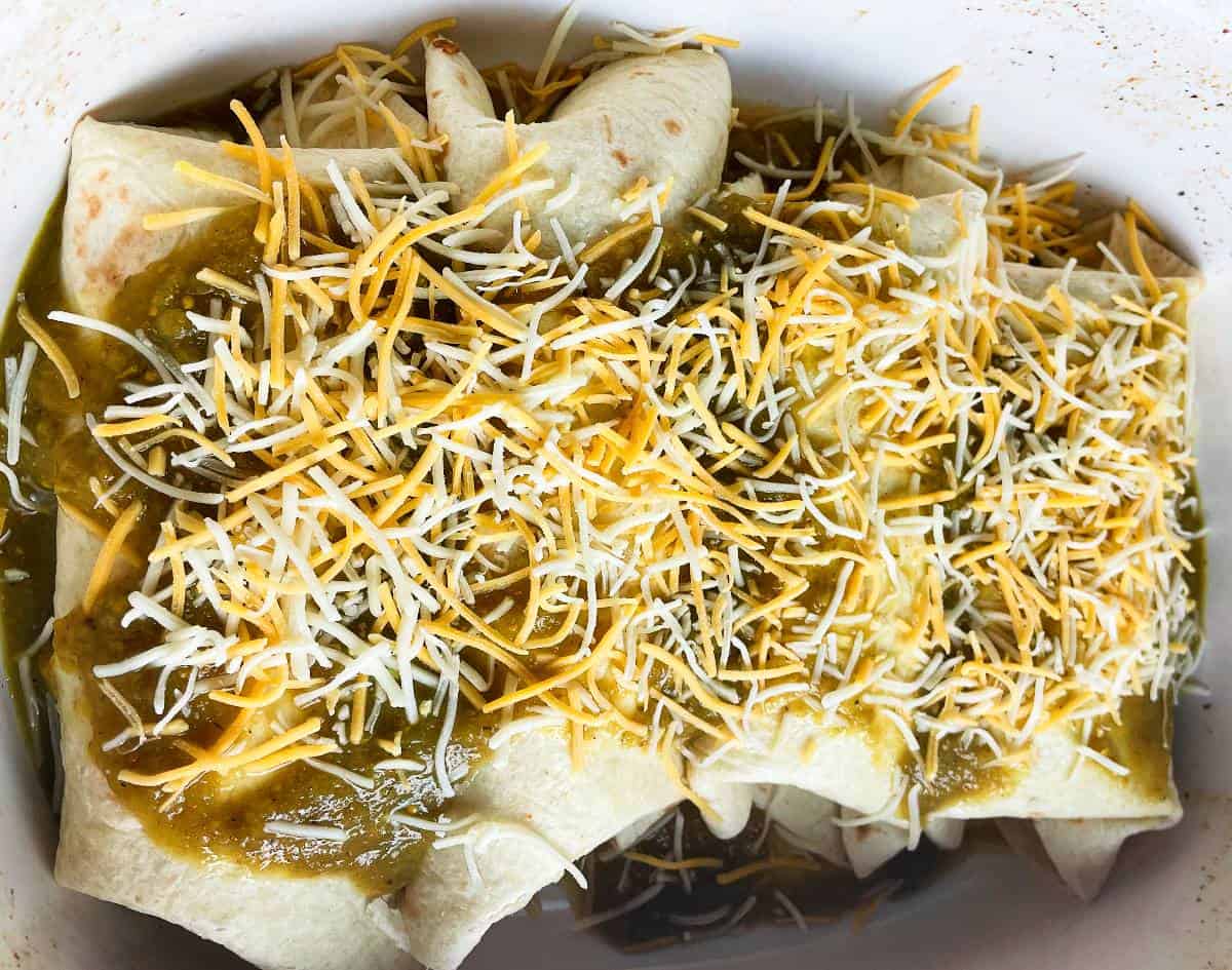 enchiladas in a baking dish before cooking, covered with green sauce and shredded cheese.