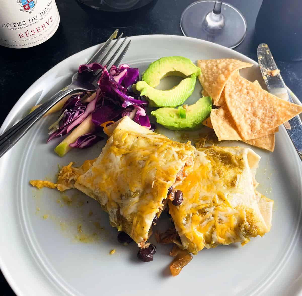 chicken and black bean enchilada cut in half, served with cabbage slaw and avocado slices, with a glass of red wine.
