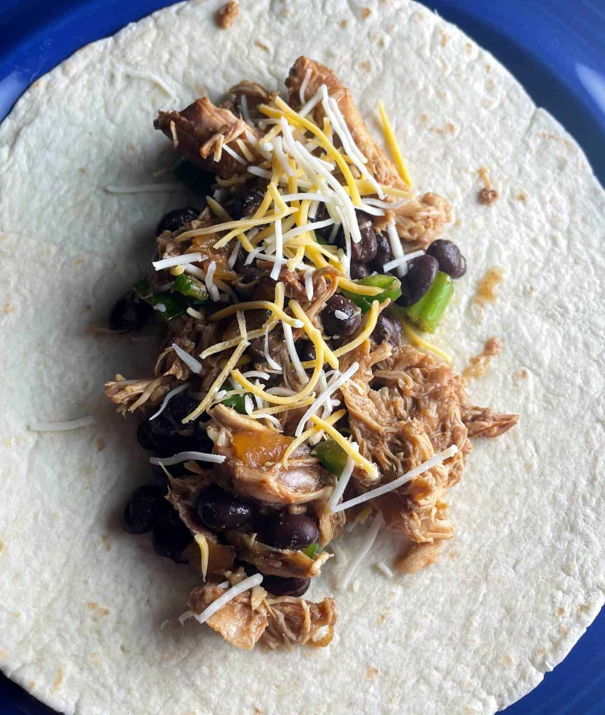 chicken and black bean filling on the middle of a tortilla shell, sprinkled with shredded cheese.