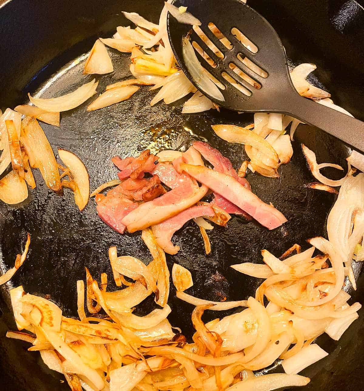 scraps of ham fat cooking with onions in a black skillet. 
