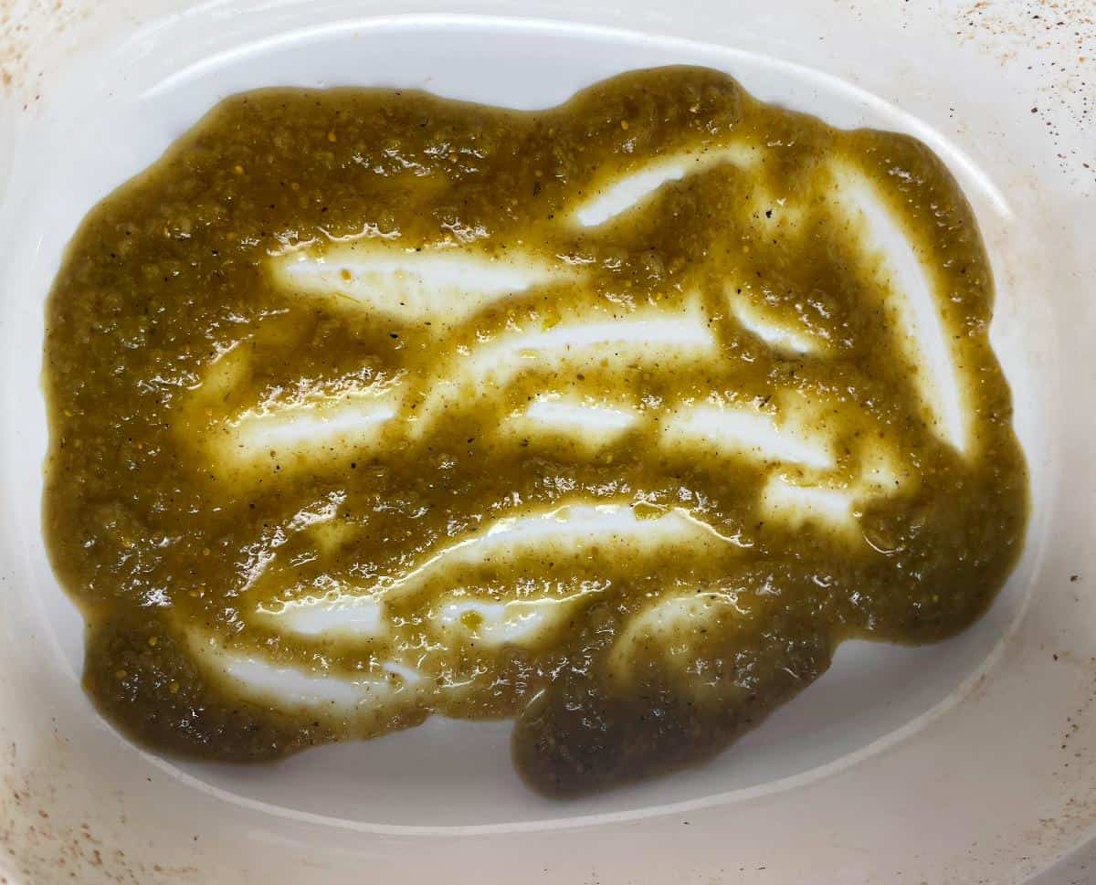 green enchilada sauce spread out on the bottom of a white casserole dish.