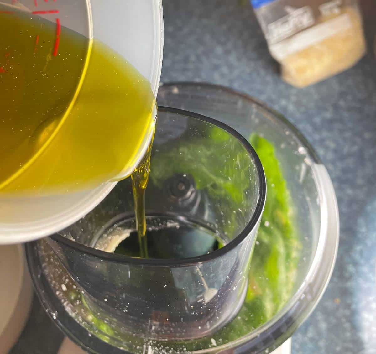 Olive oil being pour from a measuring cup into a food processor. 