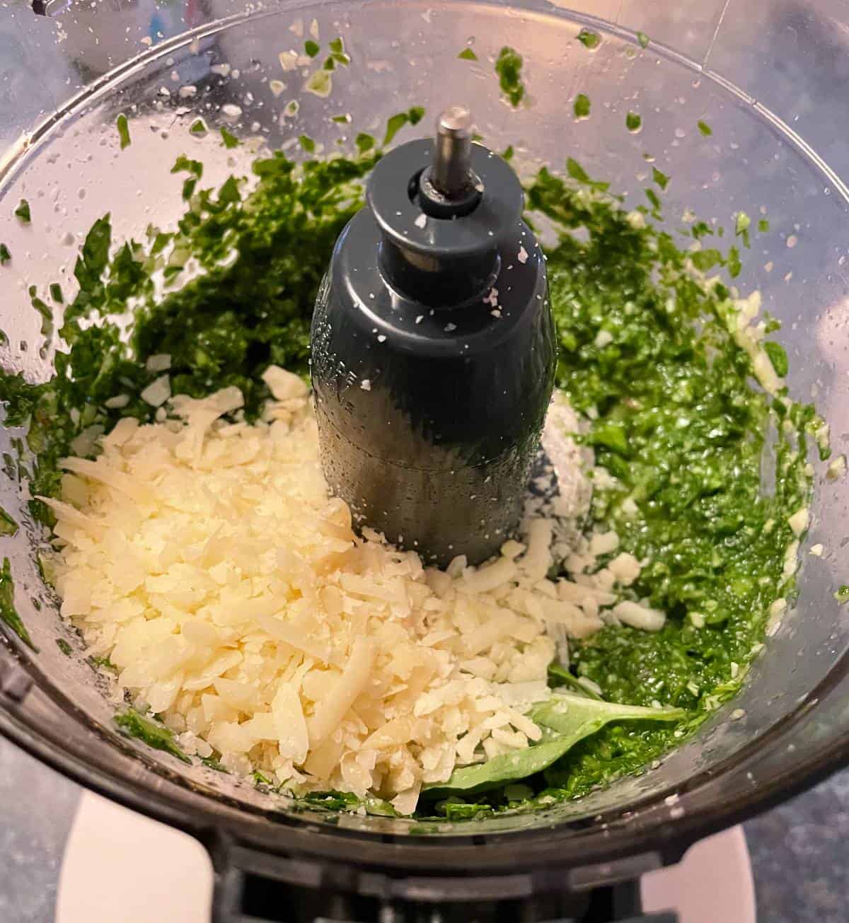 Grated parmesan cheese being added to a food processor, along with a radish green pesto puree.