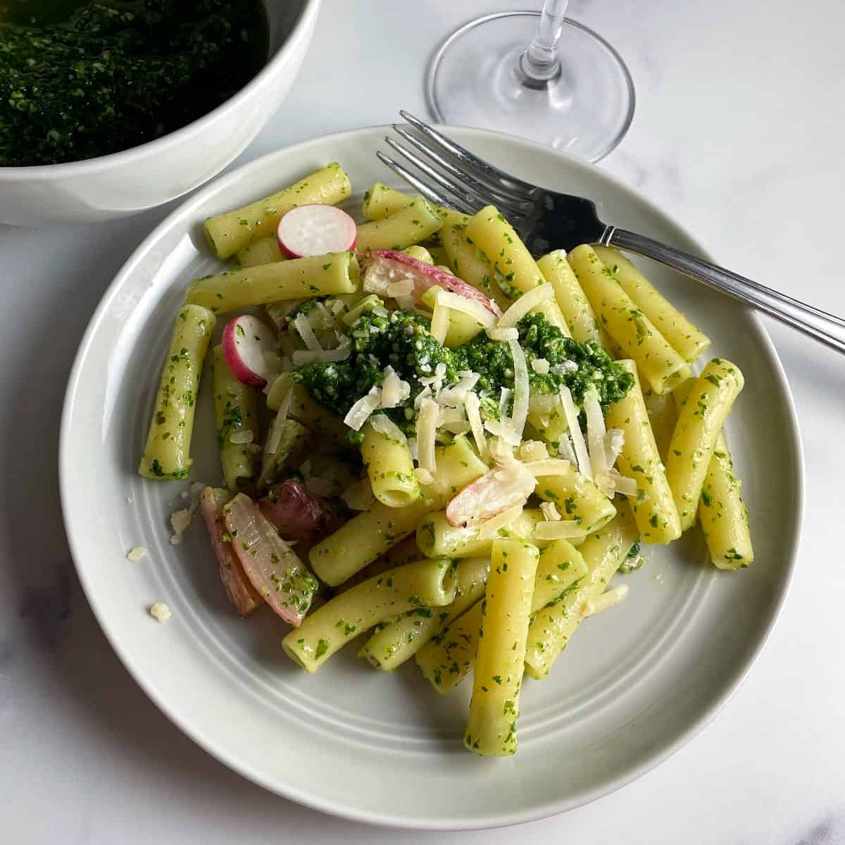 Ziti pasta on a grey plate tossed with radish green pesto and roasted radishes. 