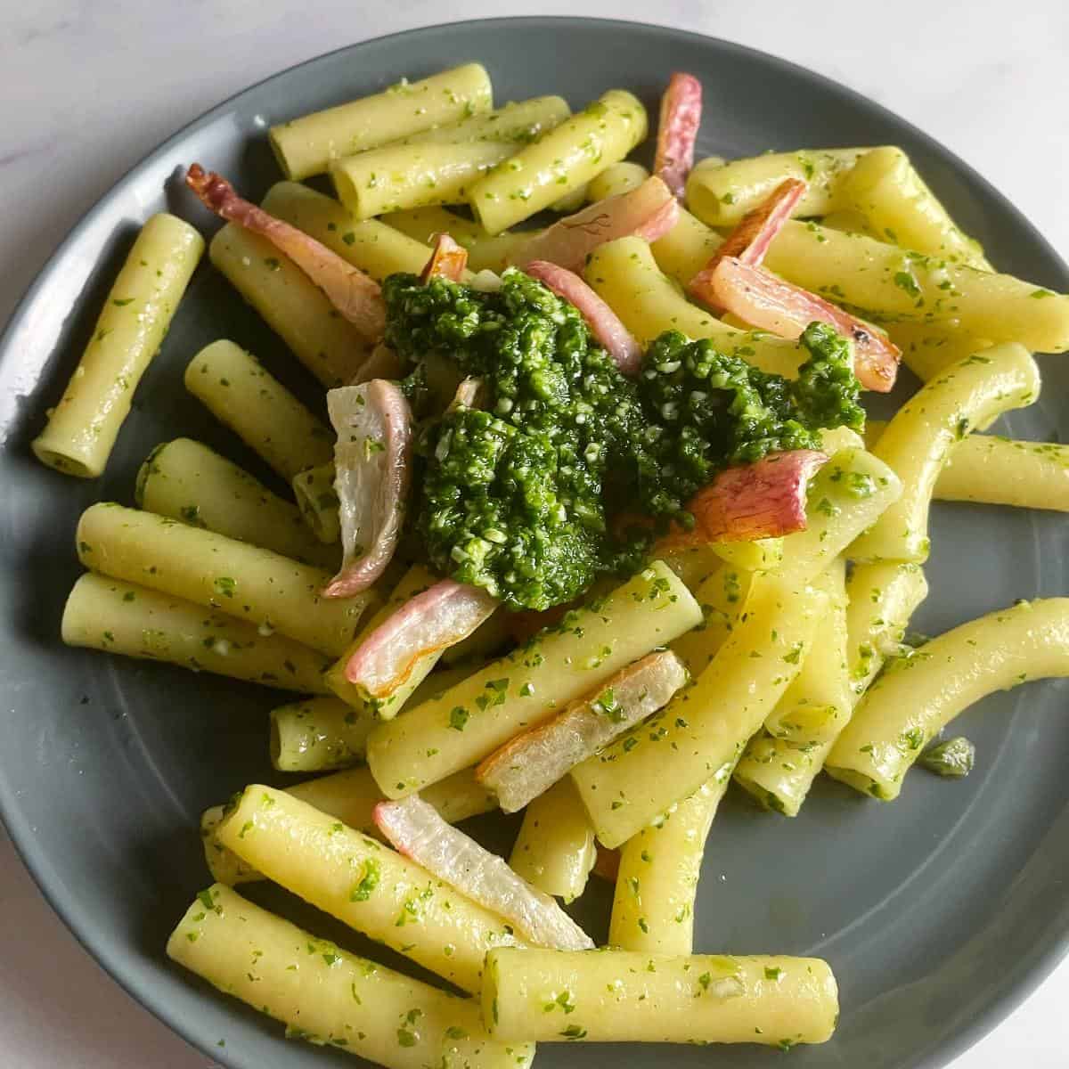 Ziti pasta tossed with radish green pesto and roasted radishes, on a dark gray plate.
