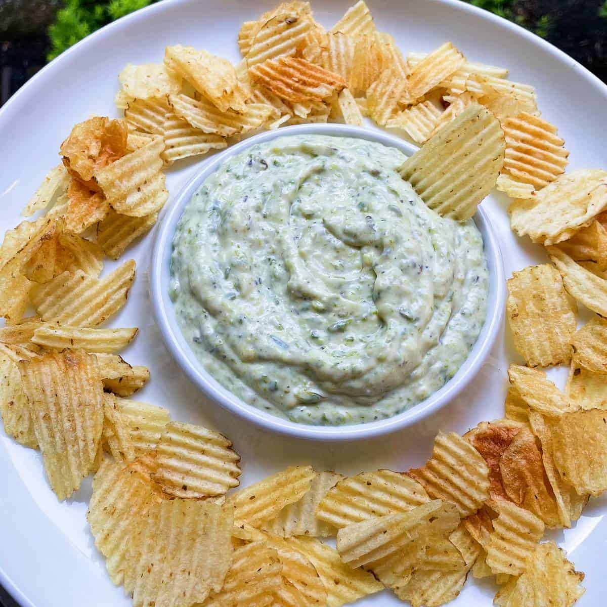 close up photo of roasted asparagus dip, served in a white bowl with potato chips.