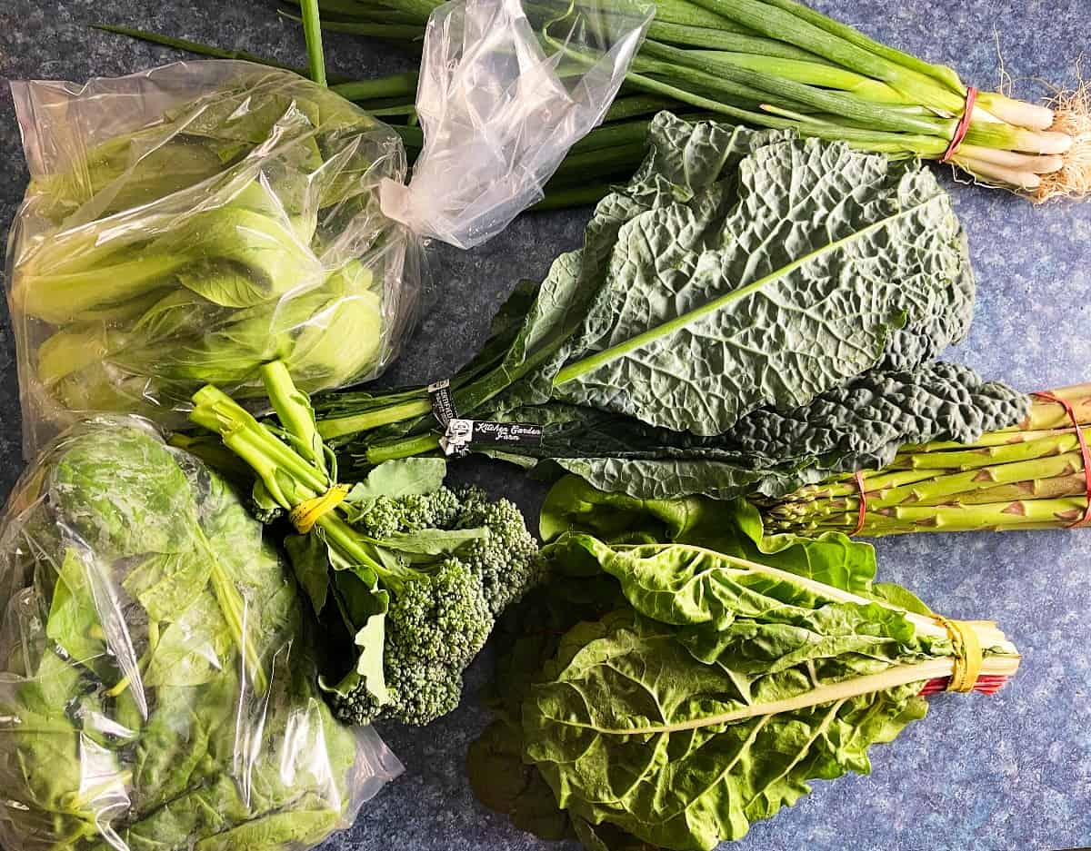 vegetables from a local farm share arranged on a counter, including bok choy, kale, scallions and baby broccoli.
