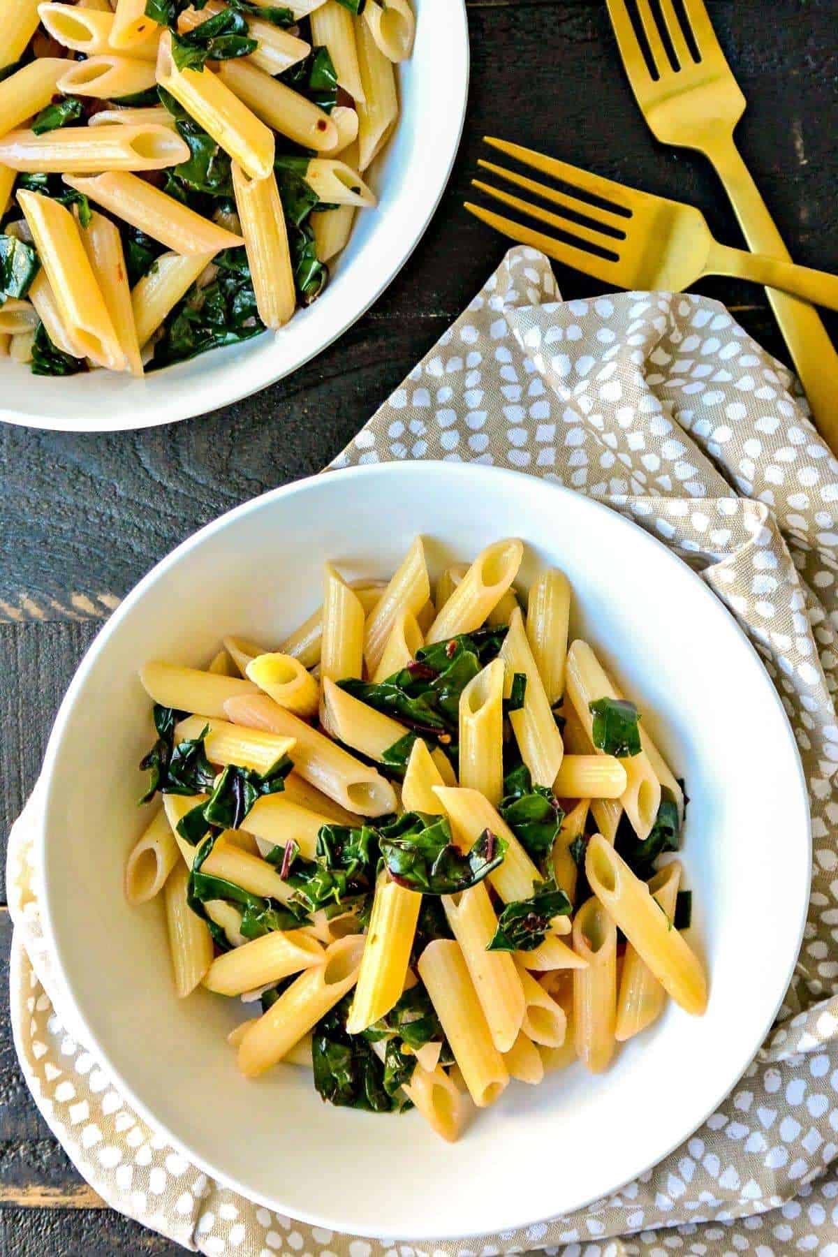 penne pasta tossed with Swiss chard and garlic, served in a white bowl.