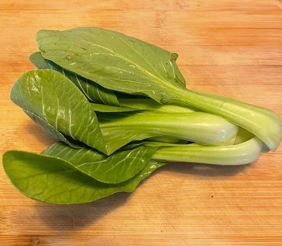 A bunch of bok choy on a wooden cutting board.
