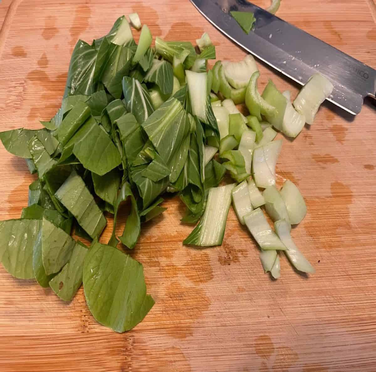 Chopped bok choy into small pieces on a wood cutting board.