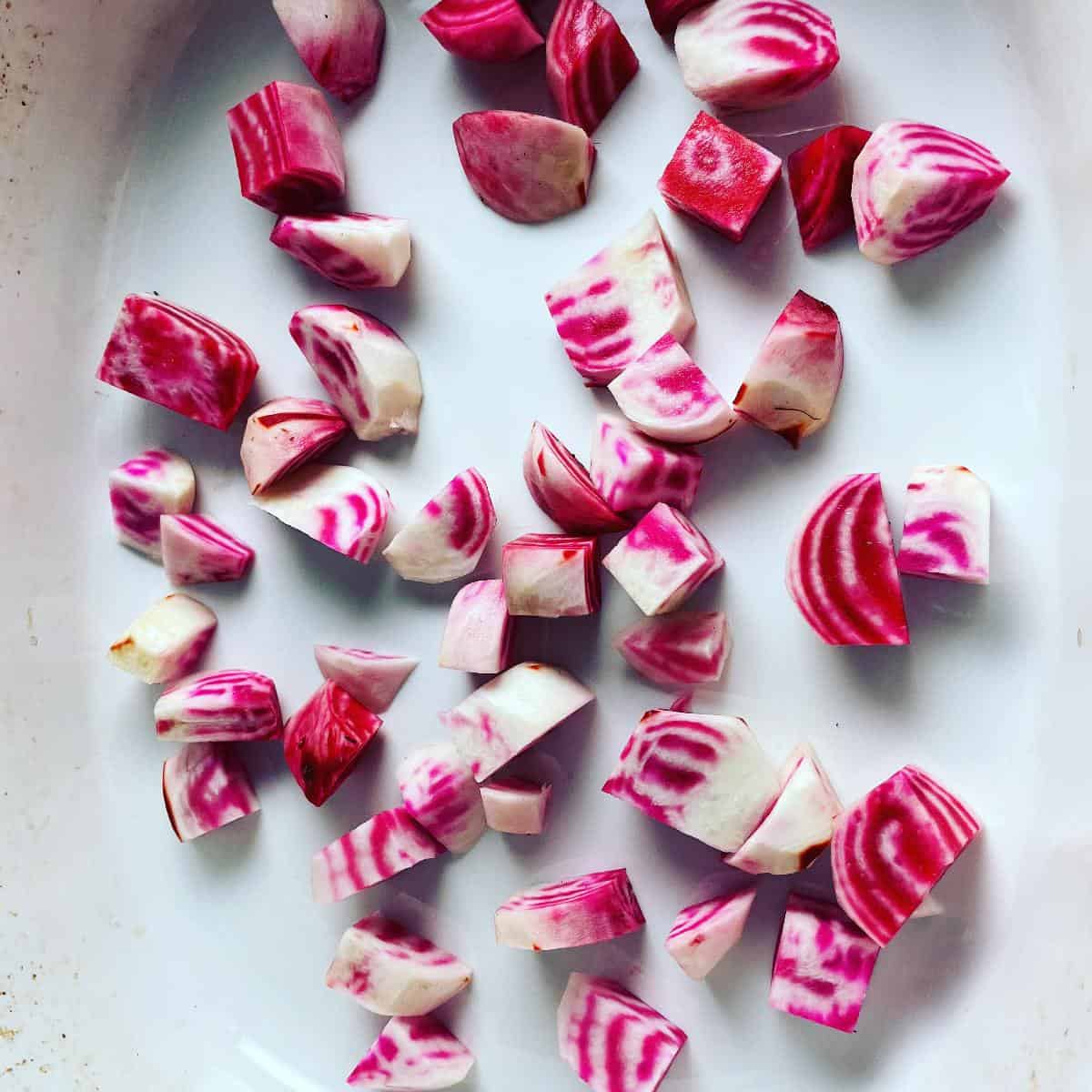 Chopped chioggia beets, with red and white stripes, in a white roasting pan.