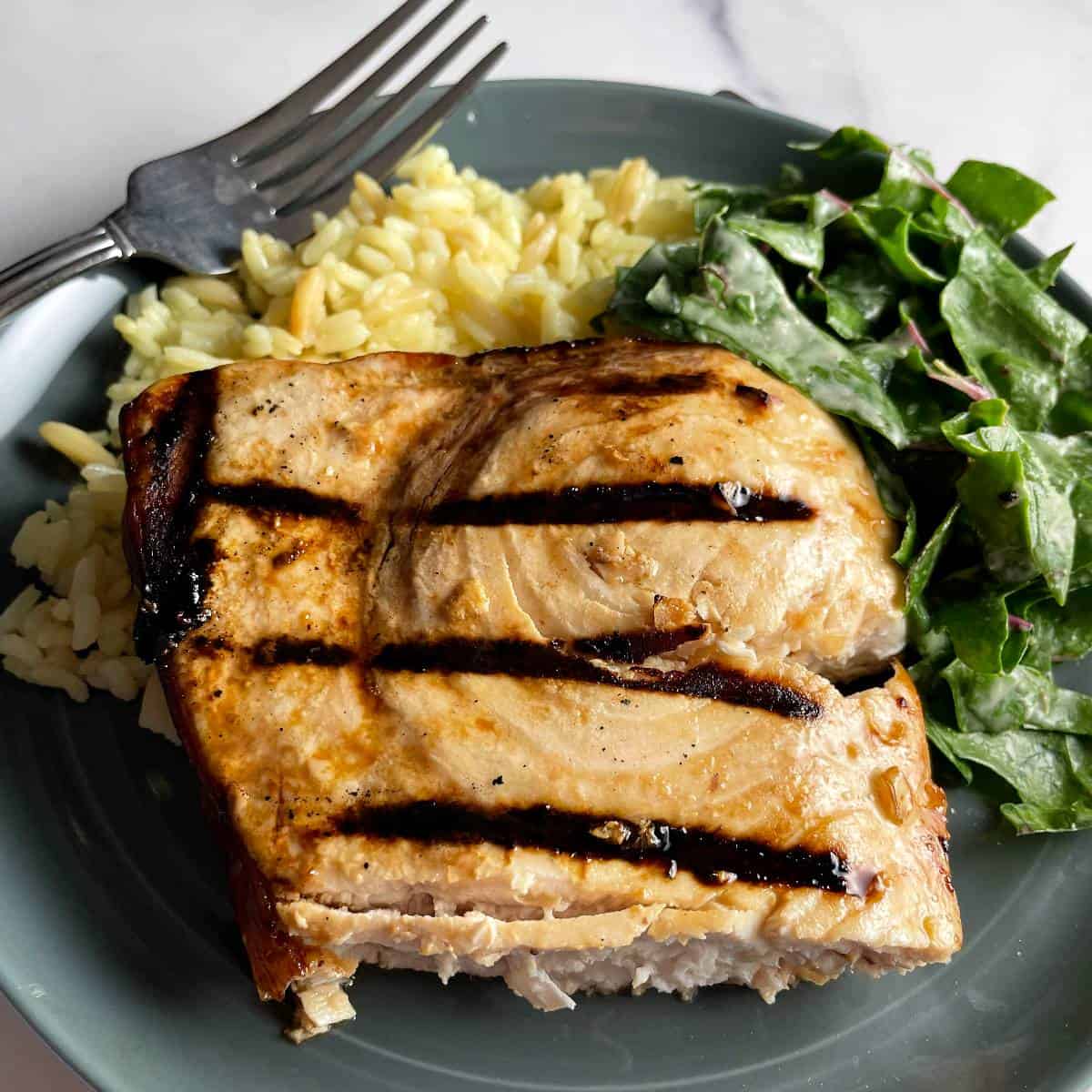 a piece of grilled swordfish served with rice pilaf and a chard salad.