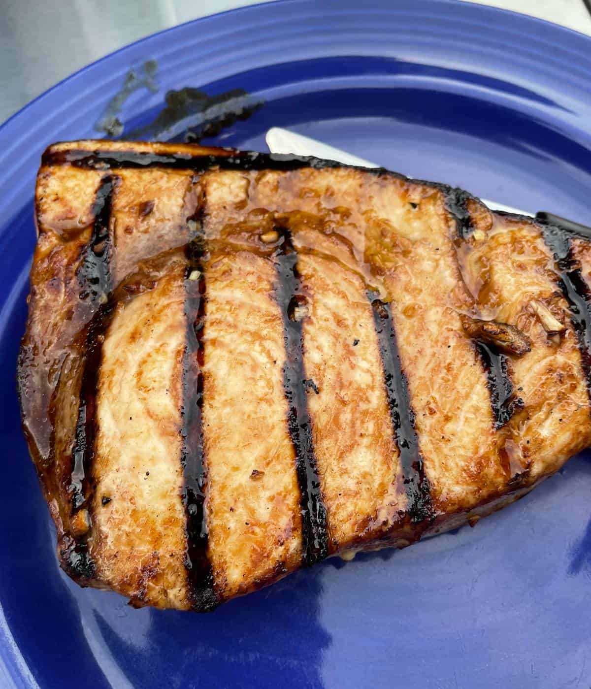 grilled swordfish resting on a blue plate before serving.