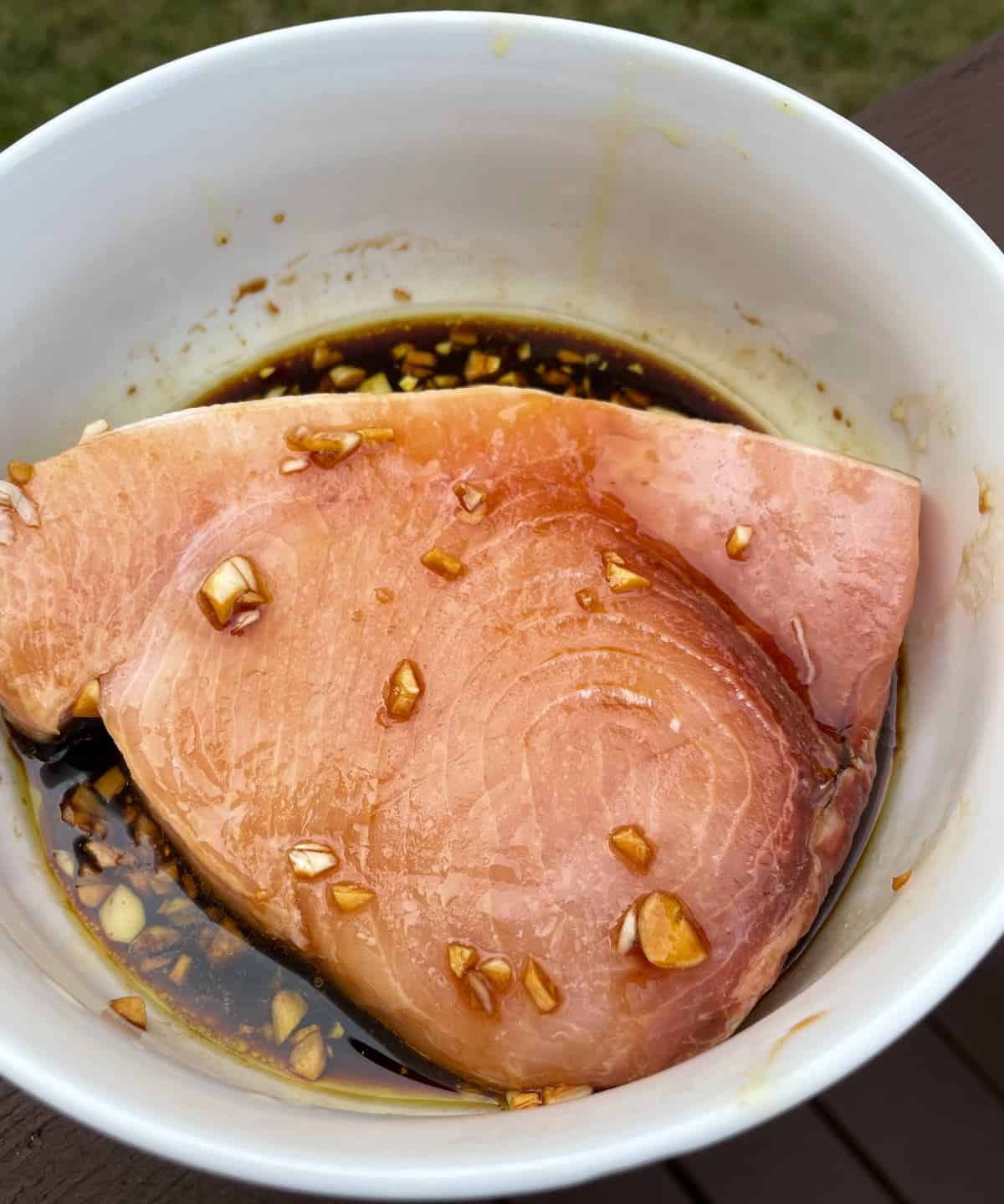a piece of swordfish steak in a white bowl with garlic soy marinade.