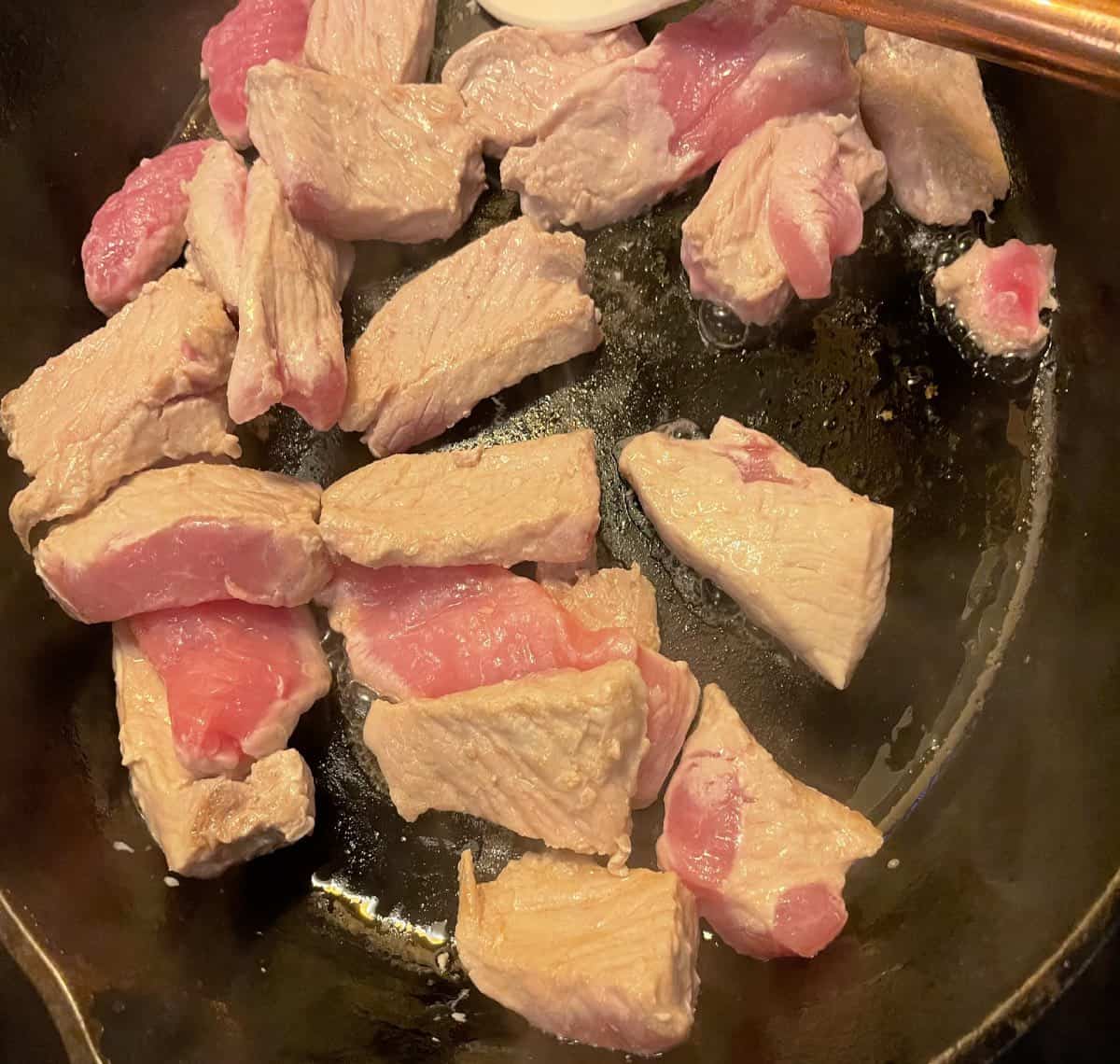 A close up of pork chop pieces cooking in a frying pan. 