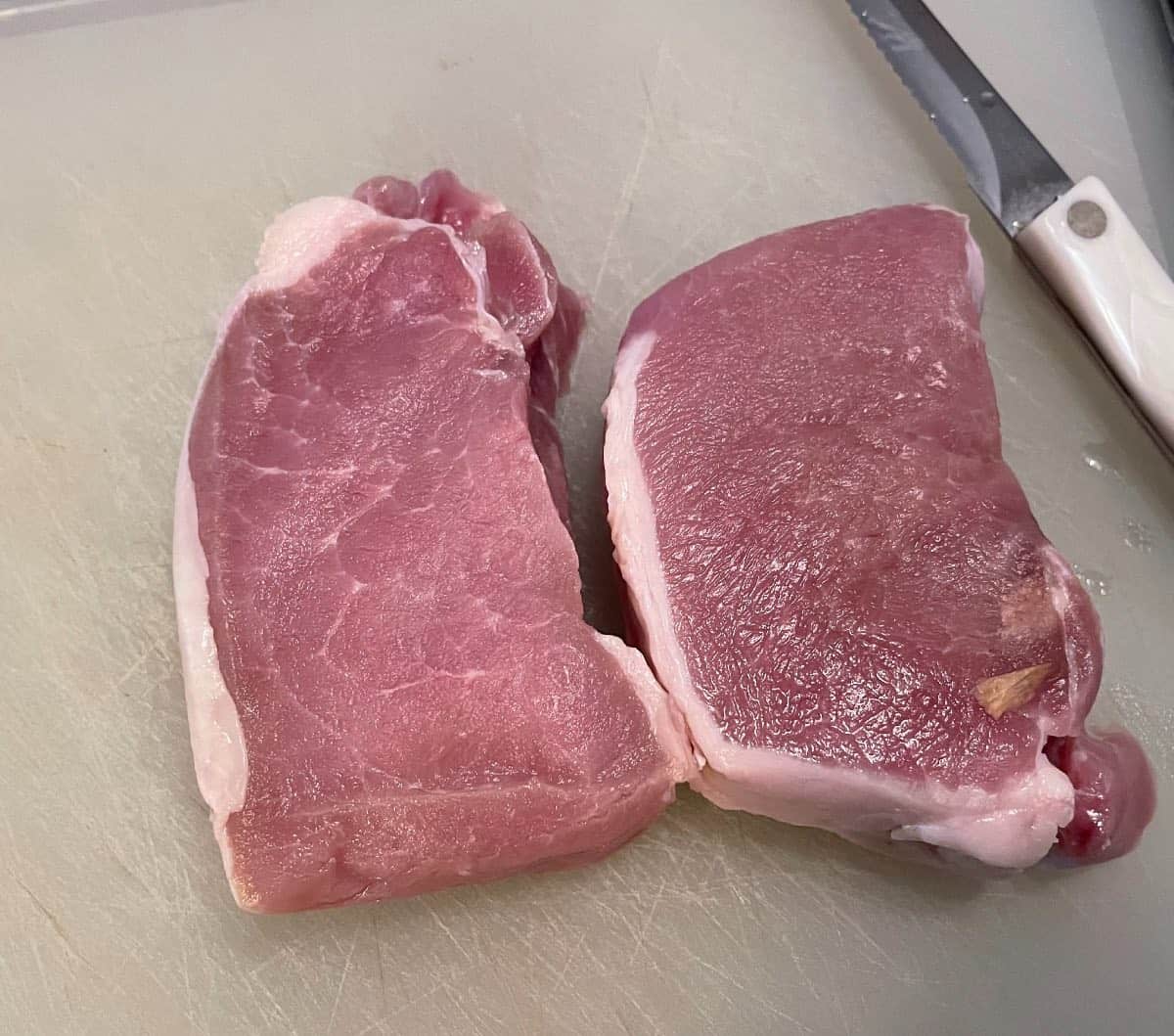 Two pork chops on a white cutting board.
