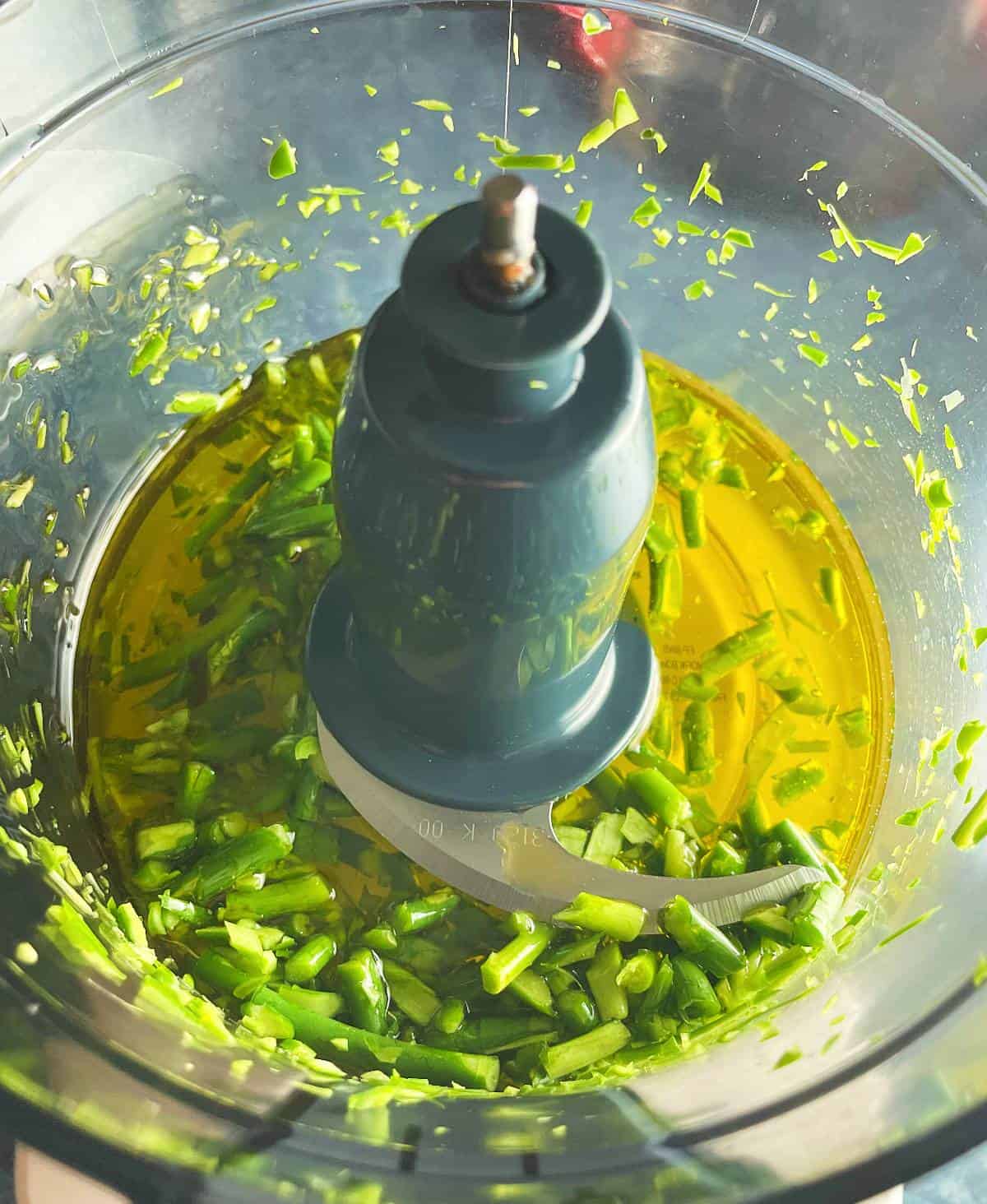 extra virgin olive oil added to a food processor with garlic scapes. 