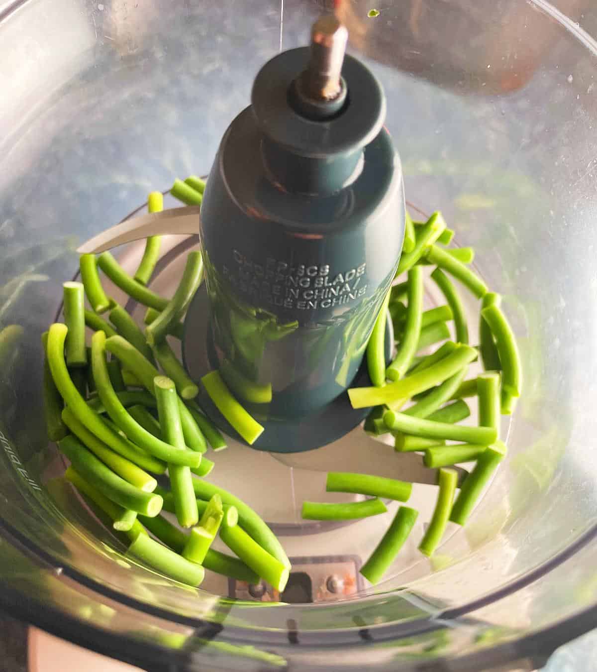 pieces of garlic scapes in a food processor.