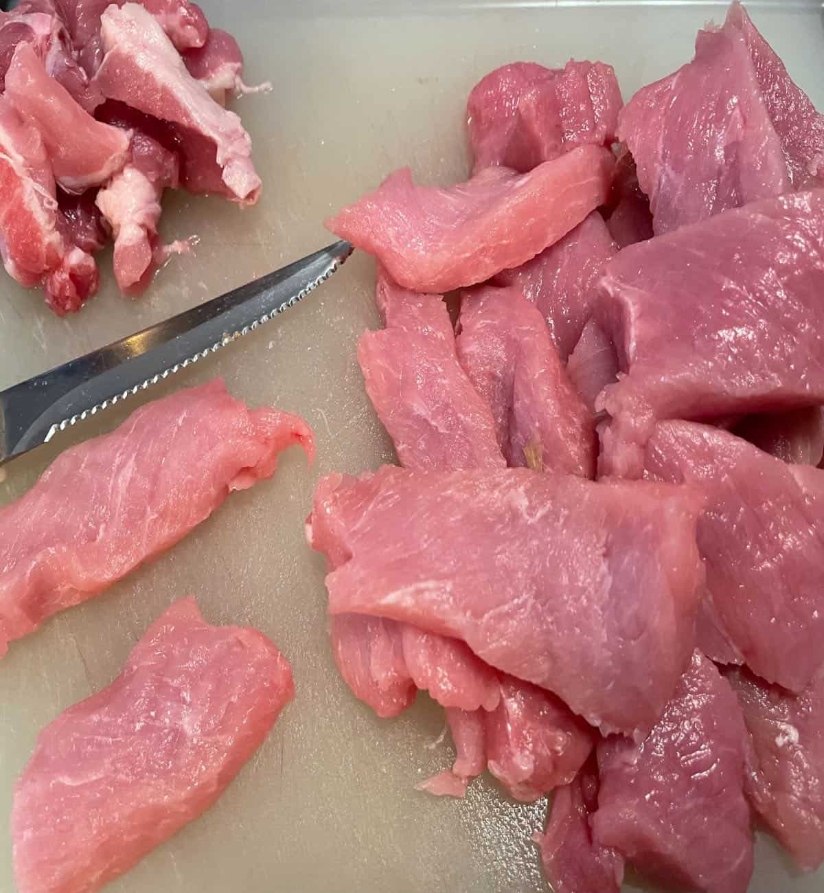 Sliced small pieces of pork chops on a cutting board with the fat removed.