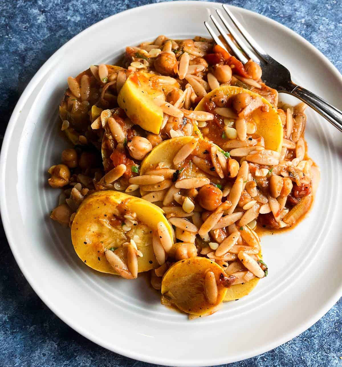 summer squash cooked with tomatoes and chickpeas, served with orzo on a light gray plate. 