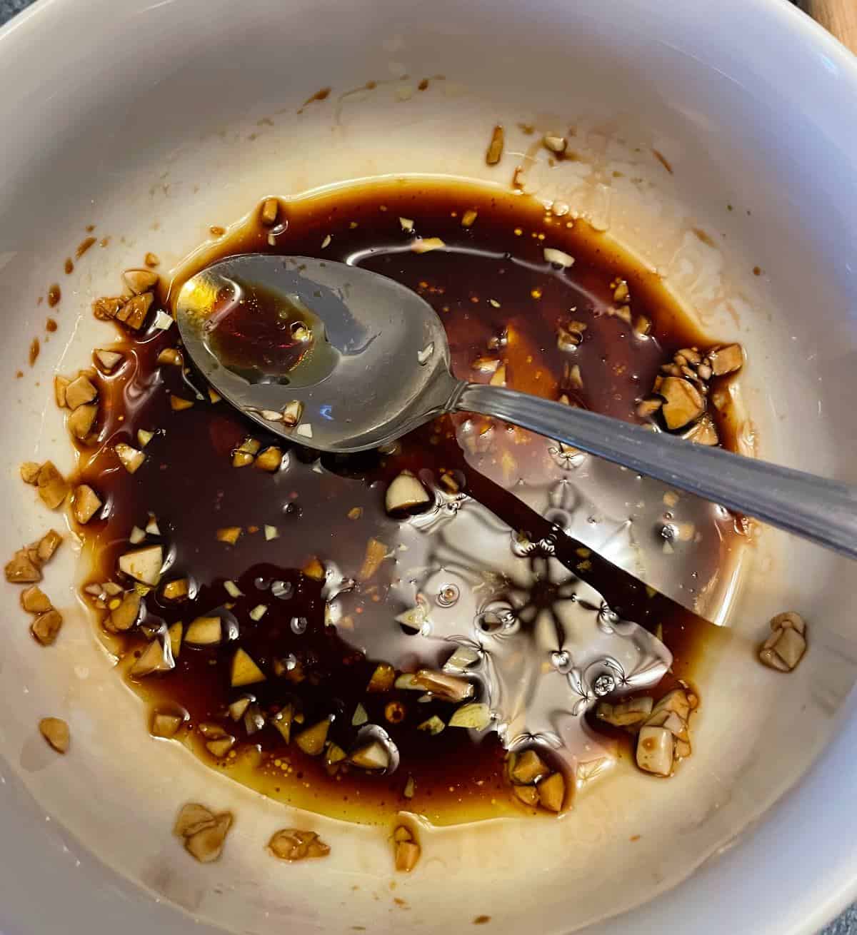 mixing soy sauce with minced garlic in a white bowl to make a swordfish marinade.