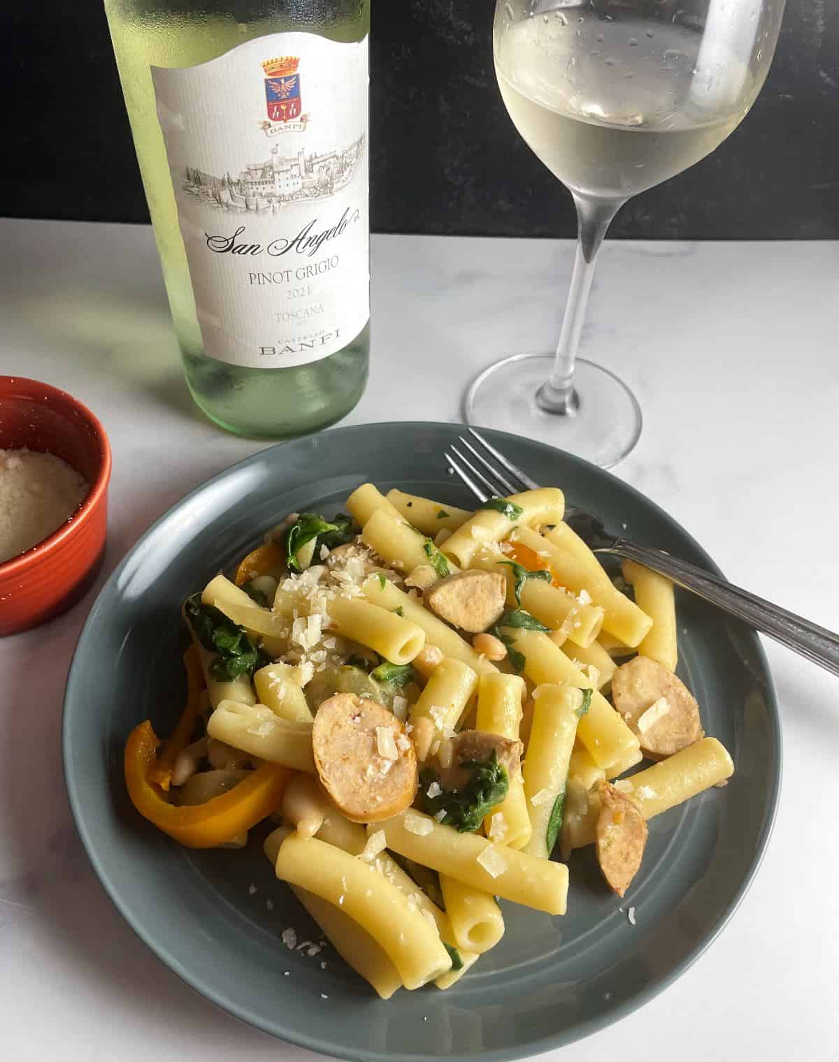 Andouille sausage pasta served on a plate along with a bottle of Pinot Grigio.