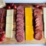 alternating rows of salami and cheese on a wooden board.
