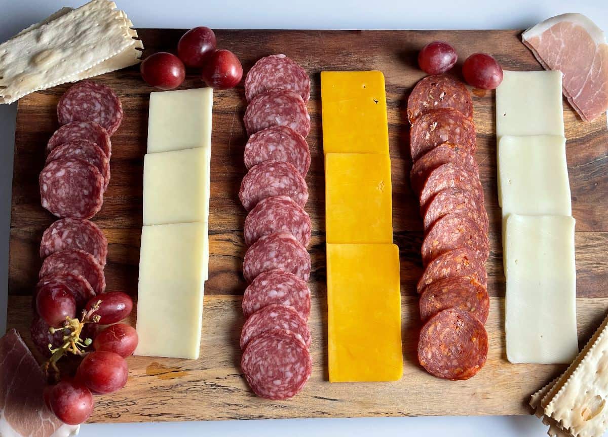 A salami and cheese board shot from overhead, with alternating rows of salami and cheese, with crackers on the edge of the board. 