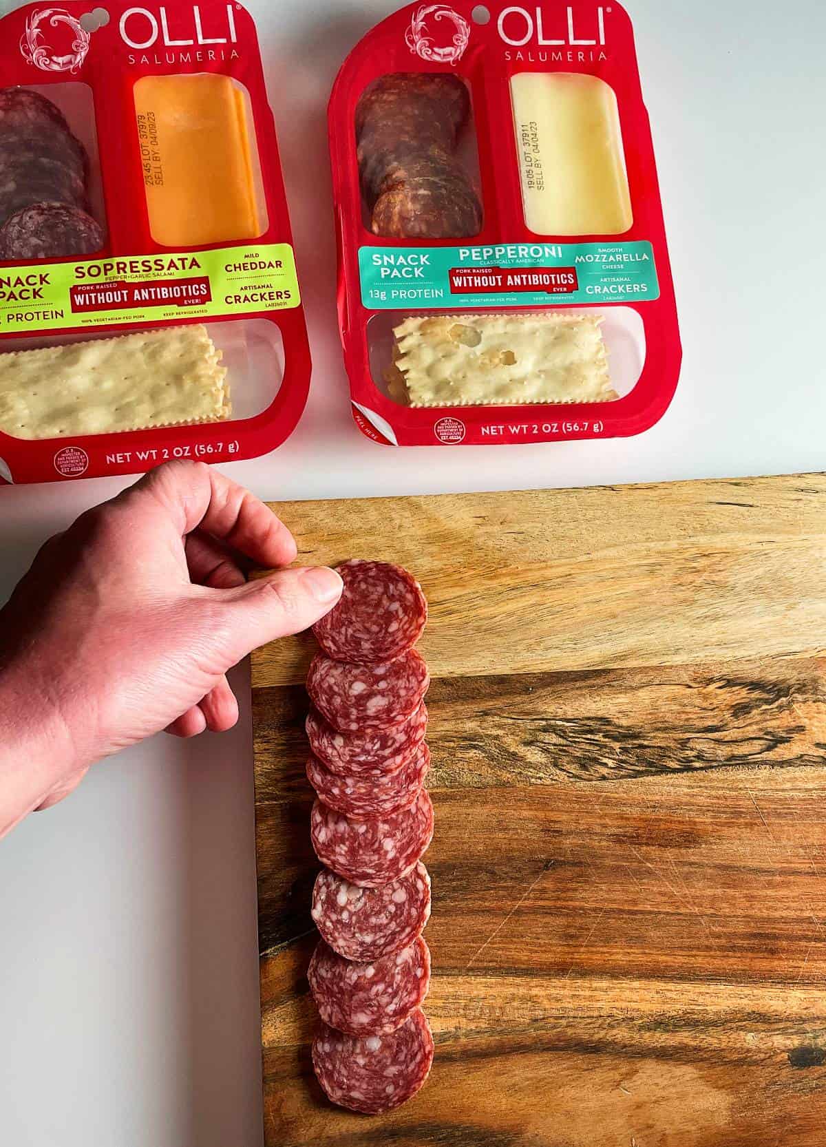 a hand shown arranging salami on a wooden board. 