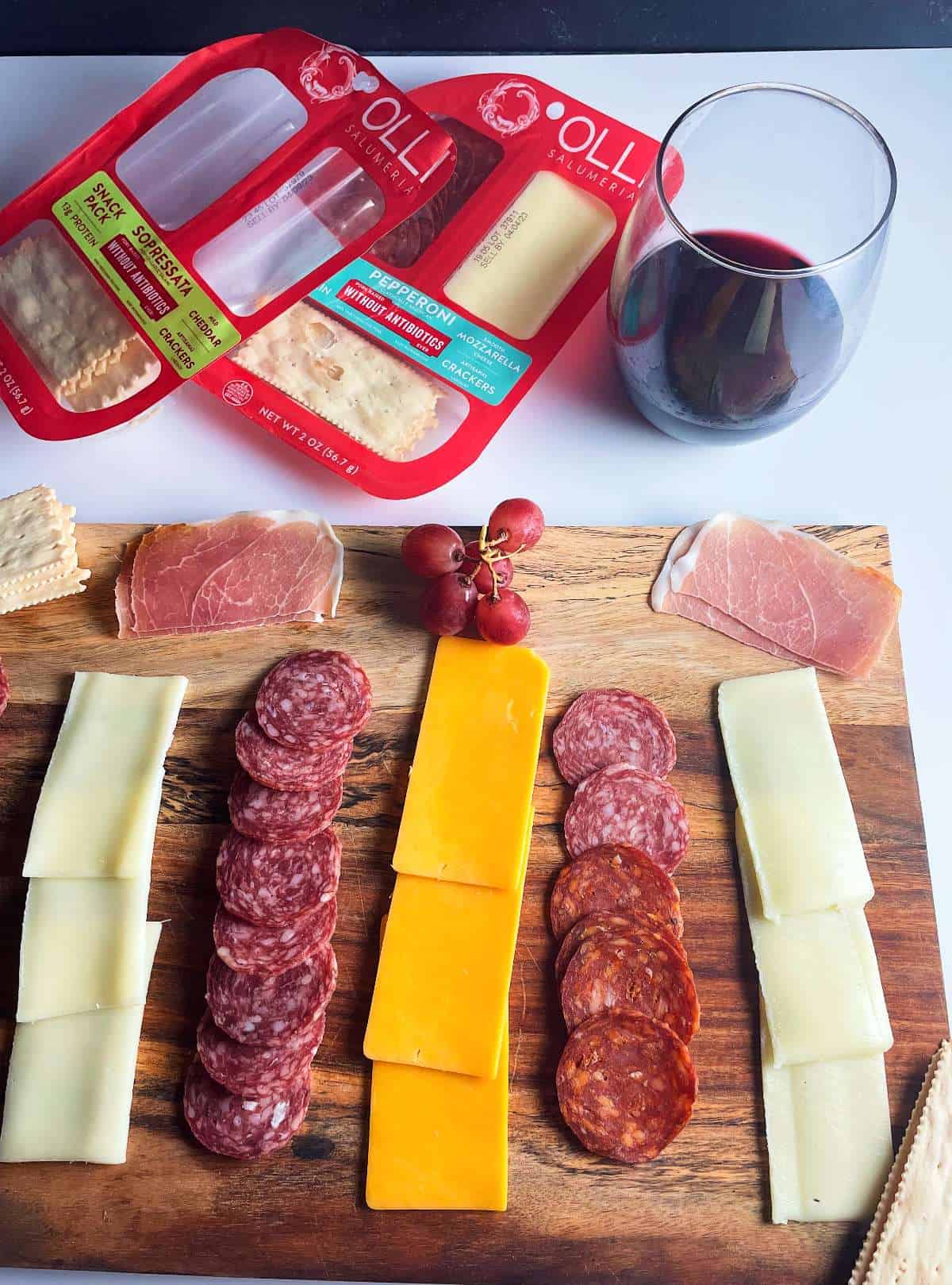 a charcuterie board with Olli Salumeria Snack Packs and a glass of red wine. 