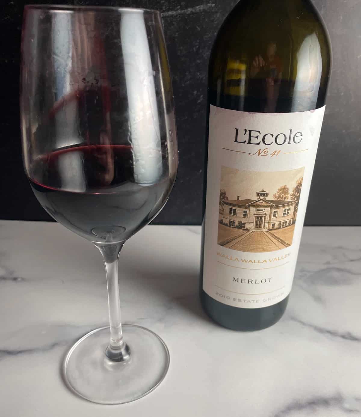 Bottle of L'Ecole No. 41 Walla Walla Merlot with a glass of the red wine alongside the bottle.