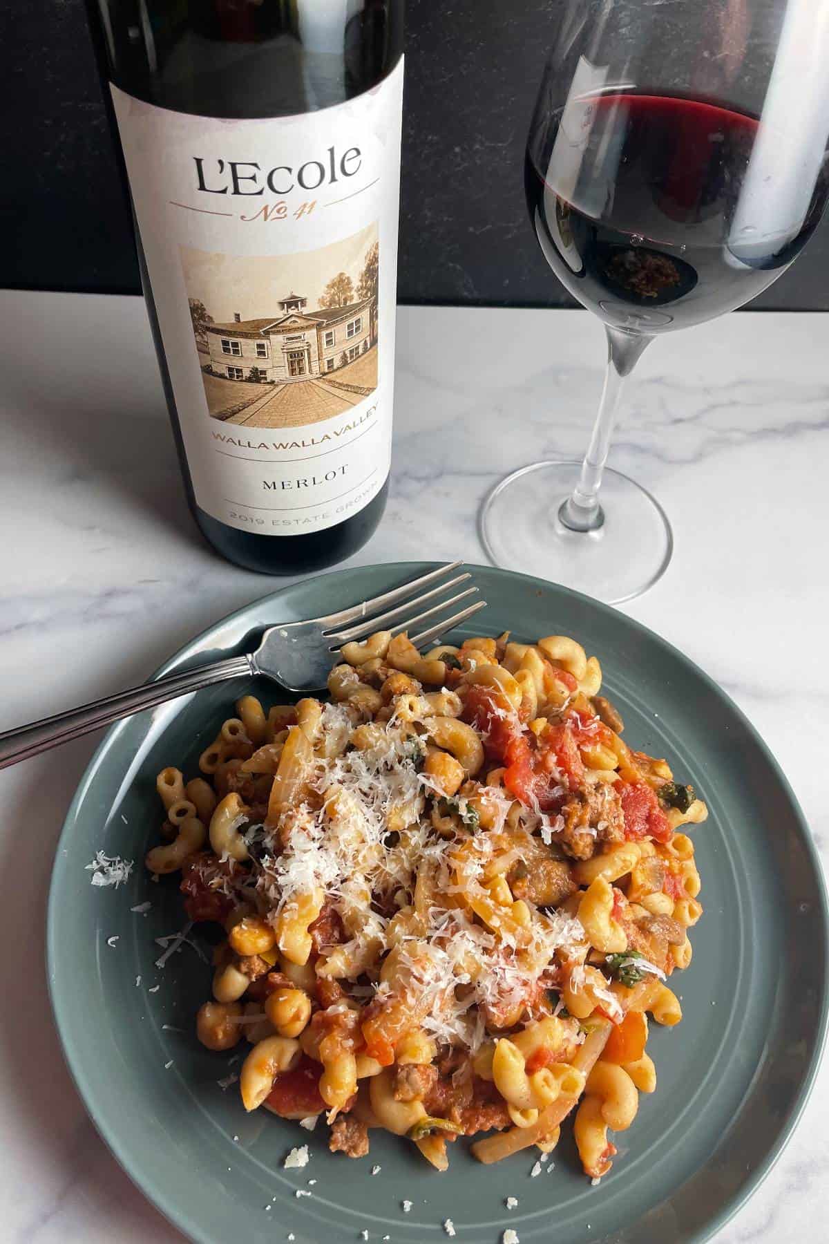 Elbow macaroni tossed with a ground beef and tomato sauce, served on a turquoise plate with a Merlot red wine.