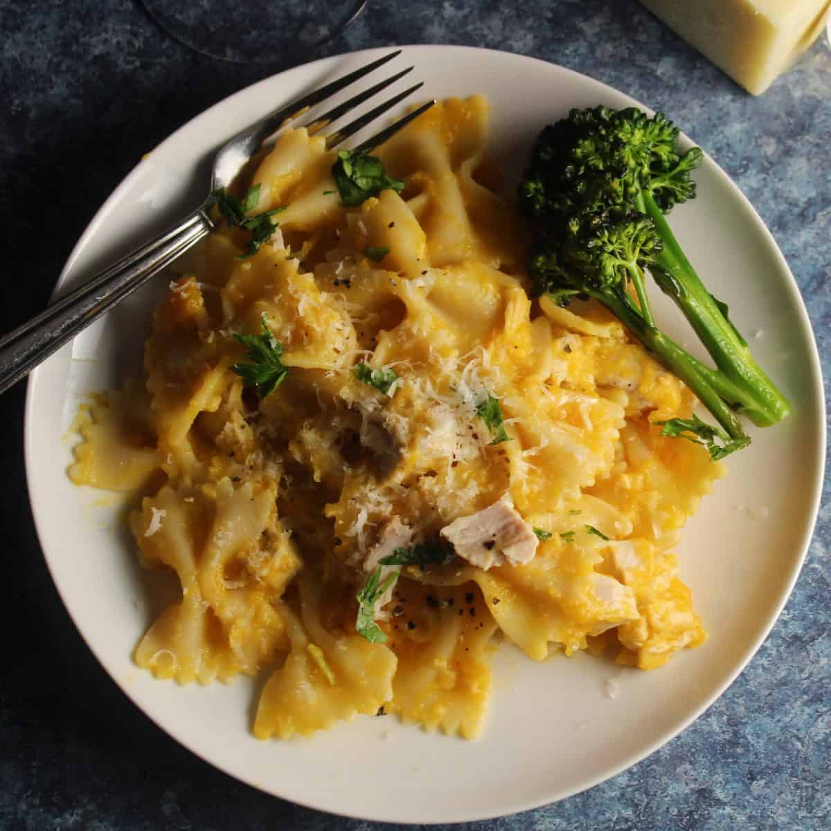 bowtie pasta with a butternut squash sauce and leftover turkey, on white plate with a side of broccoli.