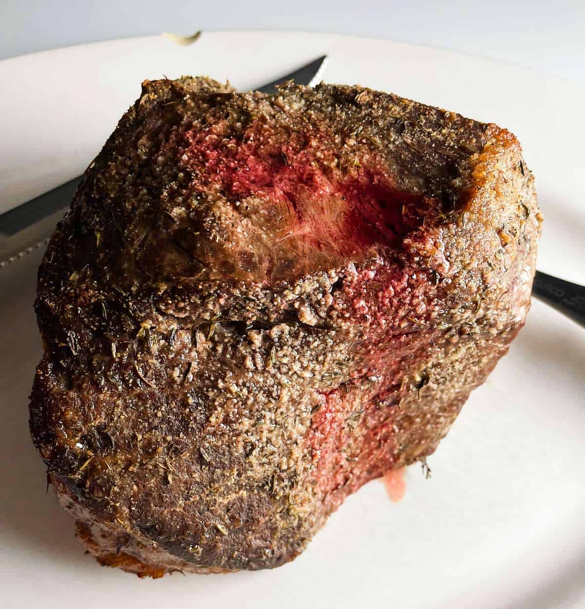 A cooked top round roast beef on a white platter, prior to slicing.