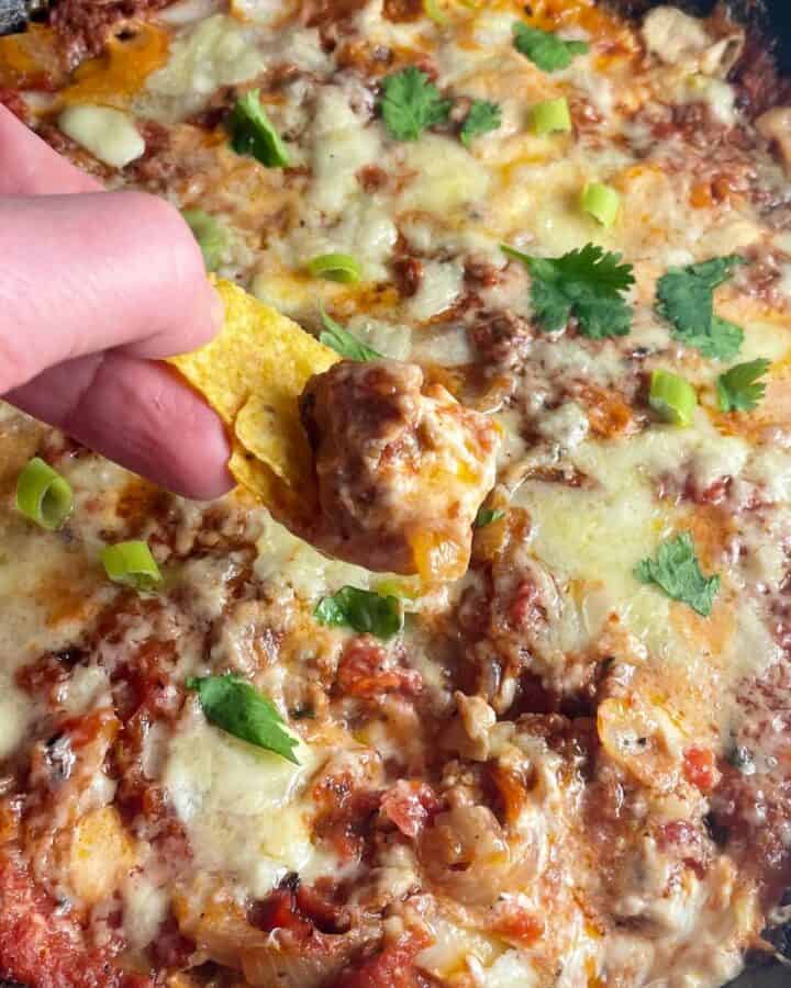 chorizo dip being scooped out of a skillet with a tortilla chip.