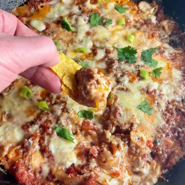 chorizo dip being scooped out of a skillet with a tortilla chip.