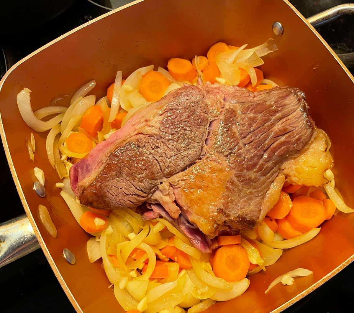 a small beef brisket in a pan with onions and carrots, after browning.