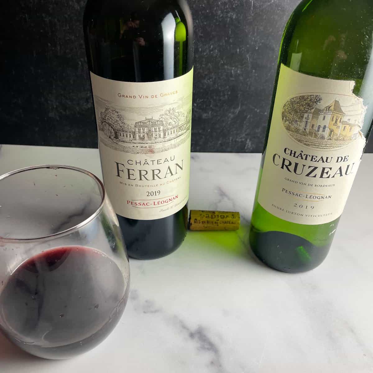 Two bottles of Pessac-Léognan wine, with a red on the left and a white on the right, and a glass of red wine.